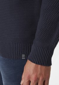 Marineblauer Strickpullover mit strukturiertem Muster an den Ärmeln, gerippten Säumen und einem kleinen "P"-Logo-Tag am Saum.