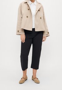 Beige kort jacka med dubbelknäppning, vit skjorta, svarta korta byxor och bruna platta skor med en liten spänndetalj.