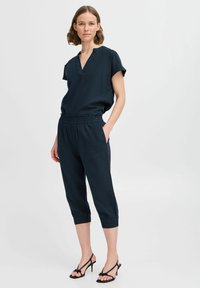 Combinaison bleu marine à manches courtes et décolleté en V, avec une taille élastique et des jambes courtes à ourlet. Design ajusté avec poches.
