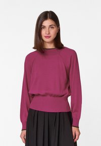 Magenta lange mouwen pullover met een ribgebreide taille en boorden, met een ontspannen pasvorm en een ronde halslijn. Zwarte rok eronder.