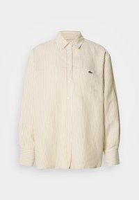 Μπλούζα με μακριά μανίκια σε ριγέ σχέδιο, σε απαλό κίτρινο και λευκό βαμβάκι, με γιακά με κουμπιά και μικρό πράσινο λογότυπο στην τσέπη στο στήθος.