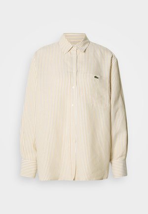 Camisa de manga larga a rayas en algodón amarillo pálido y blanco, con cuello abotonado y un pequeño logo verde en el bolsillo del pecho.