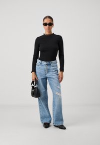 Black long-sleeve top with lace trim, high-waisted blue jeans with button closure and distressing, black handbag, and pointed toe shoes.