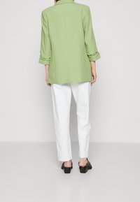 Ljusgrön kavaj med upprullade ärmar, ryggslits, i kombination med vita raka byxor och svarta klackmule. Slät tyg, skräddarsydd design.