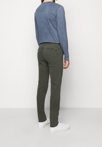 Olijfgroene broek van katoen, met een slim fit, achterzakken en een contrasterend geborduurd logo. Gepaard met een blauwe lange mouw shirt.
