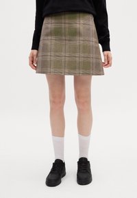 Mini gonna a quadri in tonalità marroni e verdi, con un design leggermente svasato, dettagli sui bottoni laterali e una texture morbida. Abbinata a calzini bianchi e sneakers nere.