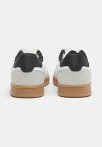 Weiße Sneakers mit einem glatten Lederoberteil und einem schwarzen Lederakzent an der Ferse sowie einer Gummirauledersohle. Strukturierte Oberfläche.