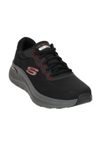 Scarpe sportive nere con tomaia in rete, dettagli rossi e suola grigia imbottita. Presentano una punta arrotondata e lacci per una calzata sicura.