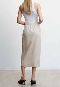 Jupe midi en lin beige avec une taille élastique, présentant une coupe droite. Portée avec un débardeur blanc ajusté et des sandales à talons brunes.