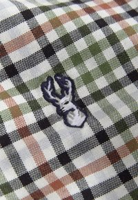 Fabric with a plaid pattern in green, brown, black, and white squares featuring a small embroidered white and dark blue lobster shape.