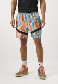 Shorts atléticos cortos con un patrón abstracto en naranja, azul y negro, hechos de un material ligero y con una cinturilla elástica.