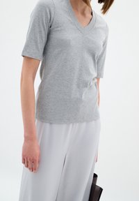 Szary, prążkowany t-shirt z dekoltem w kształcie V oraz krótkimi rękawami, zestawiony z jasnoszarymi spodniami o szerokich nogawkach i ciemną torebką.