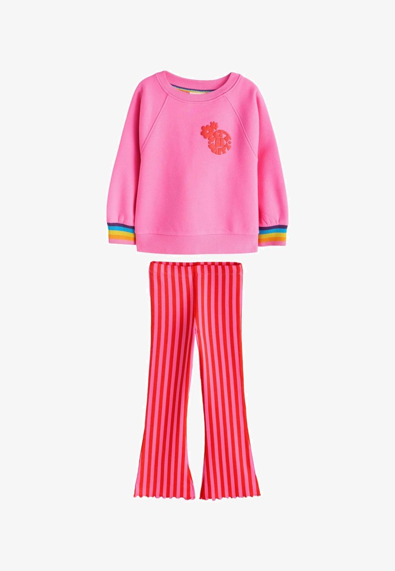 Roza majica z dolgimi rokavi z manšetami z mavričnimi črtami in cvetličnim logotipom, združena z rdečimi in roza navpičnimi črtastimi razširjenimi hlačami.