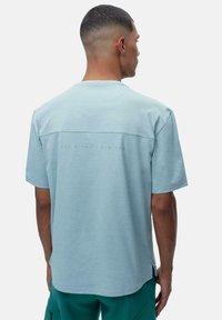 Šviesiai mėlynas trumpomis rankovėmis marškinėliai, laisvo kirpimo, su subtiliu grafiniu raštu ant nugaros ir apvaliu iškirpimu. Minkštas medvilnės mišinio audinys.