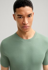 Maglione a maniche corte in maglia testurizzata di un morbido verde menta. Presenta un colletto girocollo a coste e una silhouette aderente per un aspetto elegante.