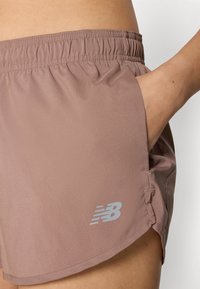 Shorts de sport rose avec une taille élastique, des poches latérales et un petit logo New Balance en argent sur l'ourlet inférieur.