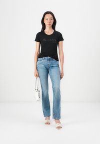 Black t-shirt with "Guess" logo, light blue jeans, white bag, and beige slide sandals. Simple, fitted design with a casual look.