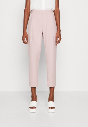 Personne portant un pantalon court rose clair et des sandales à plateforme blanches à bout ouvert, debout sur un fond blanc uni.