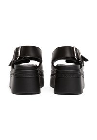 Sandale cu platformă negre, cu un exterior din piele netedă, curea reglabilă cu cataramă și talpă texturată cu detalii de branding ridicate.