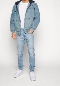 Jeansjacka med huva, ljusblå färg, texturerad tyg, matchad med ljusblå jeans och vita sneakers. Enkelt mönster och avslappnad passform.