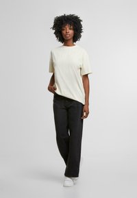 Camiseta de manga corta a rayas en color amarillo claro, combinada con pantalones anchos negros y zapatillas blancas. Textura suave, ajuste casual.