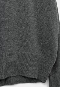 Maglione grigio lavorato a maglia con una consistenza morbida, orlo a coste e vestibilità comoda, caratterizzato da una superficie liscia e cuciture minime.