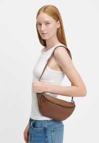 Borsa a spalla in pelle marrone con forma curva, dotata di chiusura con zip e tracolla regolabile, esposta su uno sfondo neutro.
