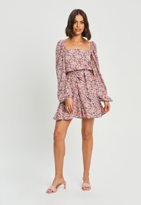 Cvečni modrček s napihnjenimi dolgimi rokavi, kvadratnim izrezom, nabrano spodnjim robom in prilegajočim pasom. Barve vključujejo rožnate, modre in bele cvetje na temni podlagi.