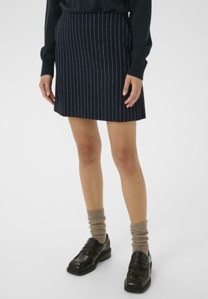 Jupe bleu marine à rayures, confectionnée dans un tissu tissé, avec une coupe droite et une taille. Associée à des mocassins noirs et des chaussettes beiges texturées.
