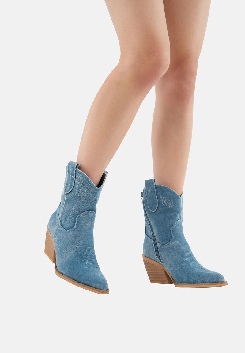 Botas de vaquero de gamuza azul con punteras puntiagudas, altura hasta la pantorrilla, costuras decorativas y un tacón apilado. Cierre con cremallera en el lateral.