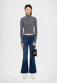 Hall hall, pika varrukaga lühike ülaosa, milles on poolkaelus; kombineeritud laiade tumedasiniste teksadega. Käes on väike must käekott hõbedaste detailidega.