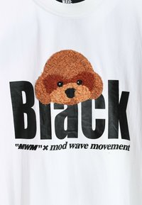 Camiseta de algodón blanca con un gran gráfico de la cara de un perro marrón texturizado y un texto en negrita de color negro que dice "Negro" con una impresión adicional más pequeña debajo.