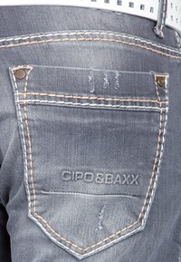 Dunkelgraue Denim-Jeans mit einer Gesäßtasche mit kontrastiertem Stich, graviertem Logo "CIPO & BAXX" und subtilen verwaschenen Details.