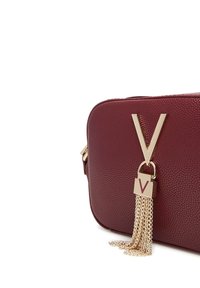 Borsa a tracolla in pelle rossa con texture, logo dorato a forma di V e dettaglio con nappina a catena. Presenta una forma rettangolare e chiusura con zip.