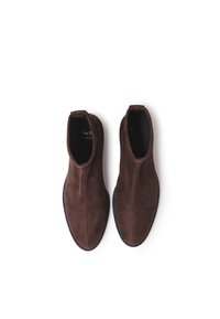 Botas de tobillo de ante marrón con puntera puntiaguda, paneles laterales elásticos y una suela negra texturizada, con un marcado mínimo en el interior.