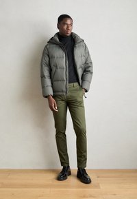 Olijfgroene pufferjack met capuchon, voorzien van een gestikte ontwerp. Gecombineerd met slim-fit donkergroene broek en zwarte veterschoenen.