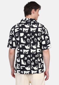 Camicetta a maniche corte con un motivo geometrico in bianco e nero, realizzata in tessuto strutturato, con colletto aperto e vestibilità rilassata.