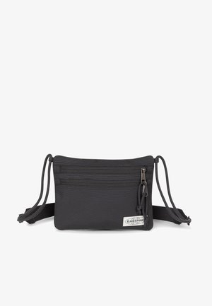 Sort stof crossbody-pung med to lynlåslommer, justerbare stropper og et logo-patch på forsiden. Kompakt og funktionelt design.