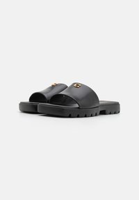Sandale negre cu talpă plată, din piele netedă, design cu vârful deschis, talpă din cauciuc și accesorii din metal auriu. Talpă groasă și texturată.