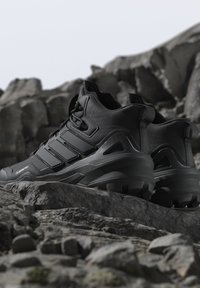 Zwarte wandelschoenen met dikke zolen op rotsachtig terrein, met nadruk op duurzaamheid en buitenshuis gebruik.