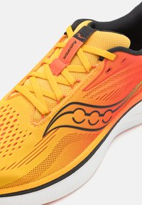 Baskets de course jaunes vif et orange avec une tige en maille texturée, accents noirs et logo Saucony bien en évidence. Comprend des lacets robustes et un rembourrage confortable.