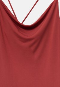 Haut rouge à col bénitier avec fines bretelles croisées. Tissu lisse et léger qui tombe doucement, arborant une couleur unie sans motifs ni accents.