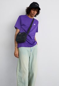 Lilla T-shirt med Nike-logo, lyseblå oversized denim bukser og en lille sort crossbody taske. Sort cap med hvid logo.