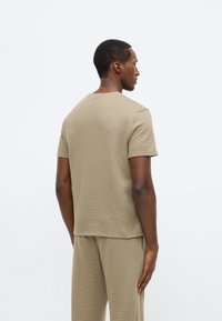 Μπεζ κοντομάνικη μπλούζα κατασκευασμένη από υφασμάτινο ύφασμα με στρογγυλή λαιμόκοψη και ευθεία βάση, συνδυασμένη με αντίστοιχα παντελόνια.