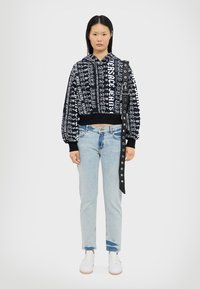 Felpa nera e bianca con design testuale, polsini ed orlo elasticizzati. Indossata con jeans a gamba dritta blu chiaro e sneakers bianche.