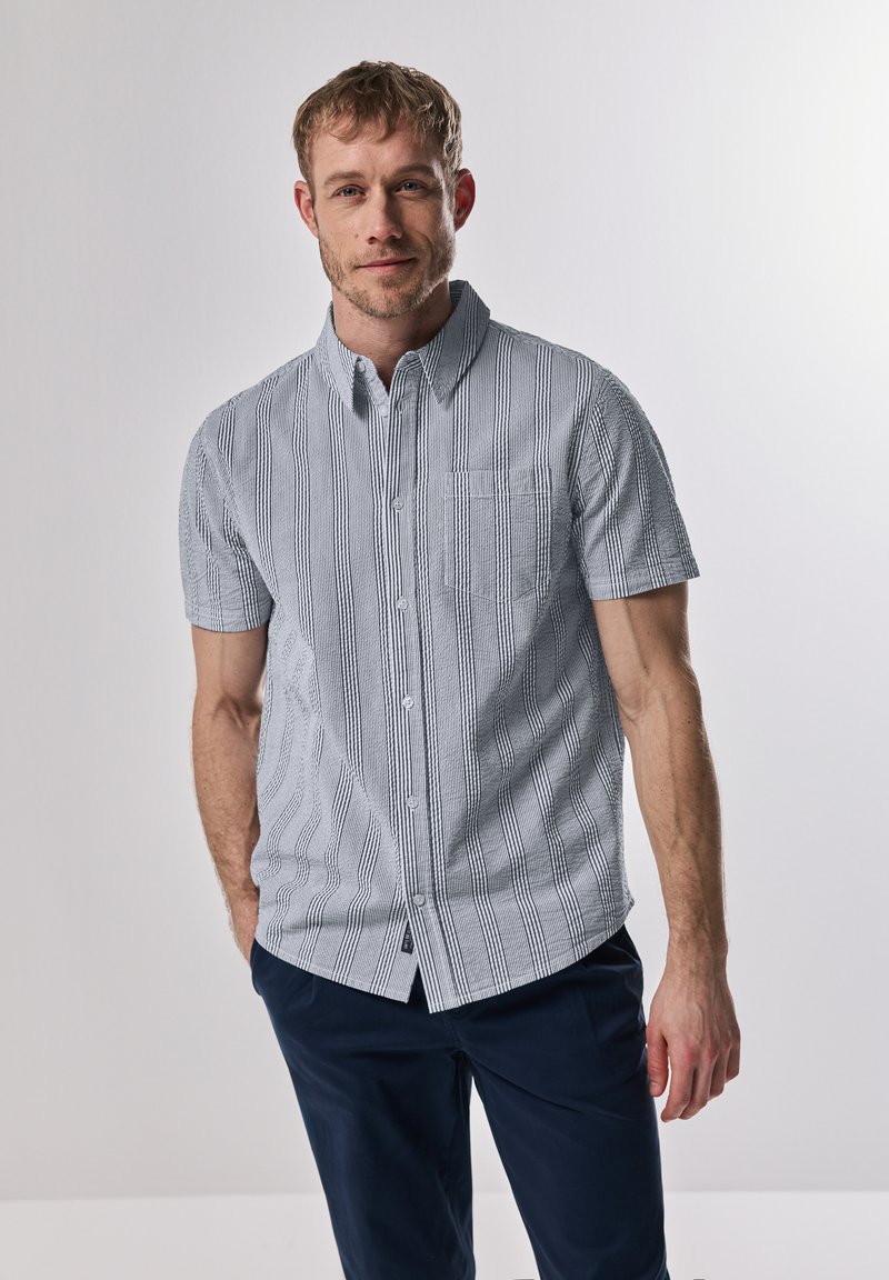 Košile na knoflíky s krátkým rukávem v světle modré barvě s vertikálními bílými pruhy. Disponuje kapsou na hrudi a detaily z texturované látky.