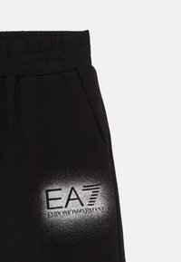 Černé tepláky z jemné látky. Mají elastický pás a velké stříbrné logo s přechodem na stehně.