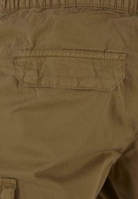 Brunt tyg med en mjuk struktur, som har en ficka med klaff på baksidan med sydda kanter. Designen är enkel och funktionell.