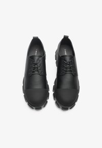 Chaussures en cuir noir avec des orteils arrondis, dotées de semelles en caoutchouc texturé, d'un design à lacets et d'une finition lisse sur la partie supérieure.