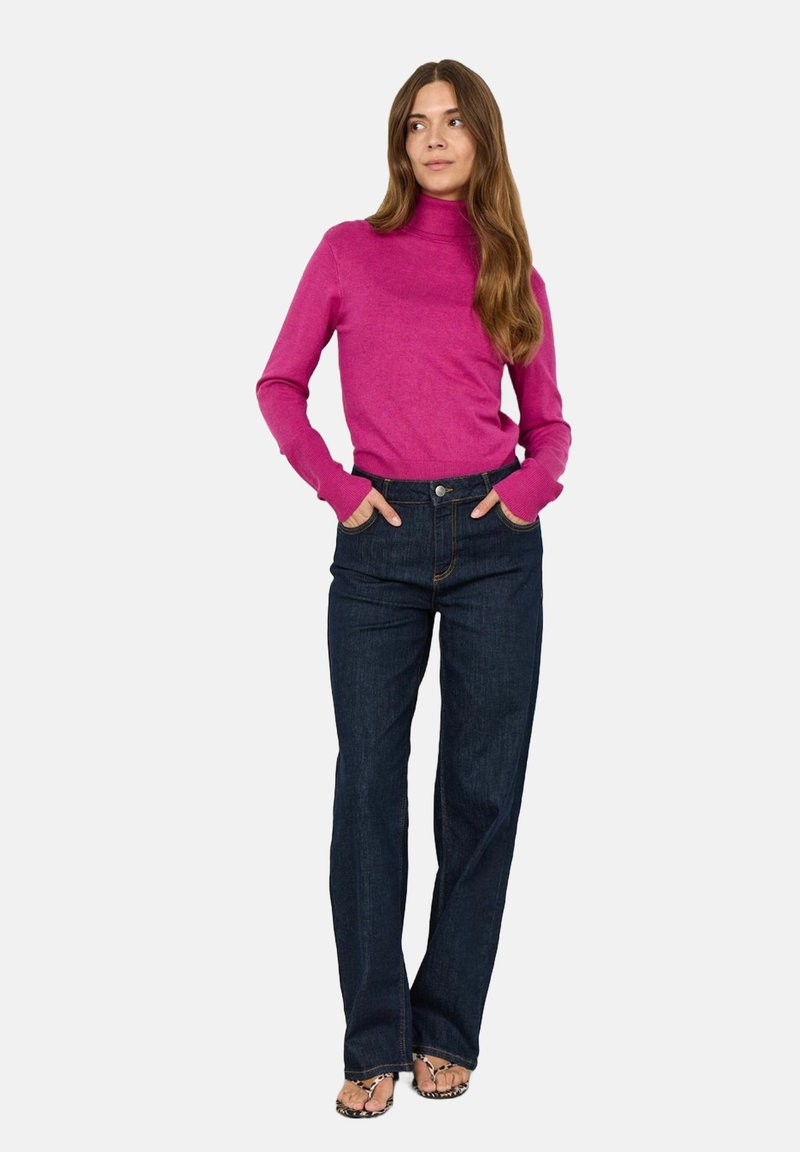 Rosa polotröja i kombination med mörkblå utsvängda jeans. Tröjan har figurnära långa ärmar och jeansen har en klassisk design med fickor.